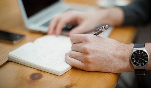 A man writing in a notepad with a pen A man writing in a notepad with a pen